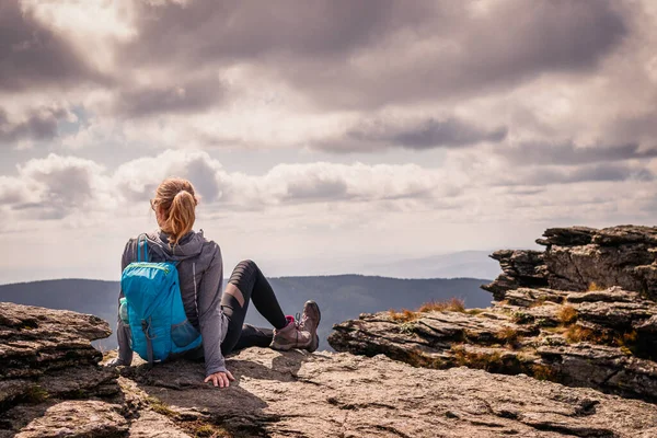 Sırt çantalı bir kadın kayanın üzerinde oturuyor ve manzaranın tadını çıkarıyor. Dağ zirvesinde turist yürüyüşü ve tırmanışı. Dağ yürüyüşü sırasında rahatlama