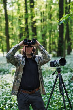 Vahşi yaşam fotoğrafçısı ormanda kuş gözlüyor. Dürbünlü bir adam bahar ormanlarında kuş arıyor.