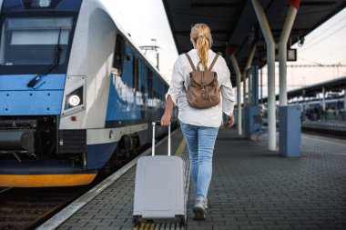 Trenle seyahat et. Bavullu bir kadın tren istasyonundaki trene binmeye gidiyor. Solo gezgin