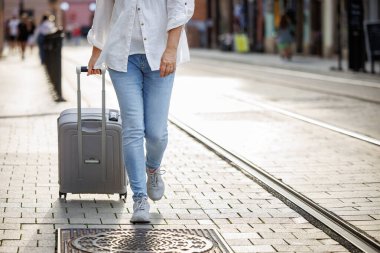 Kadın turist valiz taşıyıp şehir caddesinde yürüyor. Tek başına seyahat yaşam tarzı