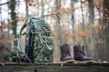 Deri çizmeli yürüyüş ekipmanları, sonbahar ormanlarında su geçirmez sırt çantası ve tripod.