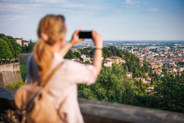 Avrupa 'da solo seyahat sırasında İtalya' nın Bergamo kentindeki Venedik duvarlarından şehir manzarası fotoğrafı çeken bir kadın turist. Arkaplana odaklan