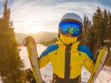 Gün batımında tepede kayakla poz veren kadın gözlükleriyle yansıyor.