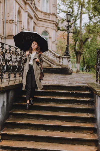 Mladá hezká žena v podzimním oblečení procházky po ulici města s deštníkem za deštivého počasí — Stock fotografie