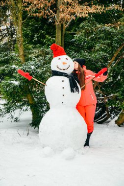 Kırmızı şapkalı ve eldivenli kardan adamla poz veren kadın. Kış tatili