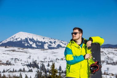 Güneş gözlüklü gülümseyen adam elinde snowboard tutuyor. Boşluğu kopyala
