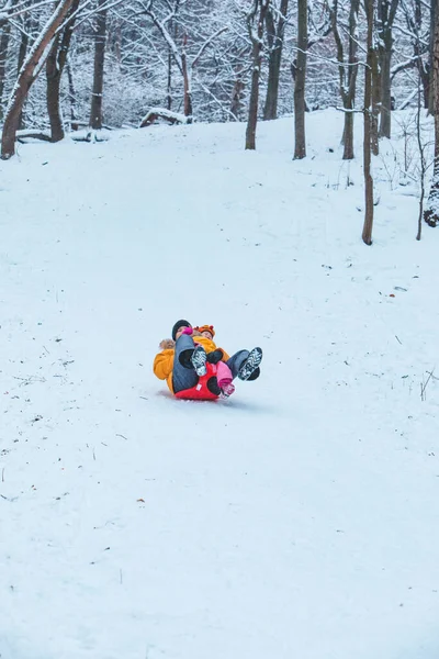 黄色い冬のコートを着た娘と一緒に雪の丘の家族の時間を滑り — ストック写真