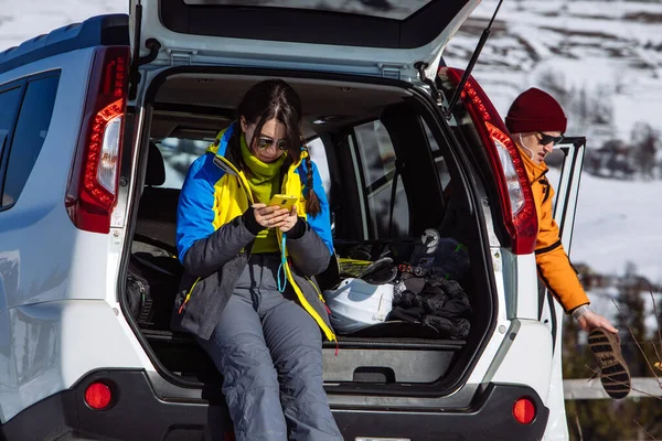 woman sitting in suv car trunk full of ski and snowboard stuff. lifestyle concept