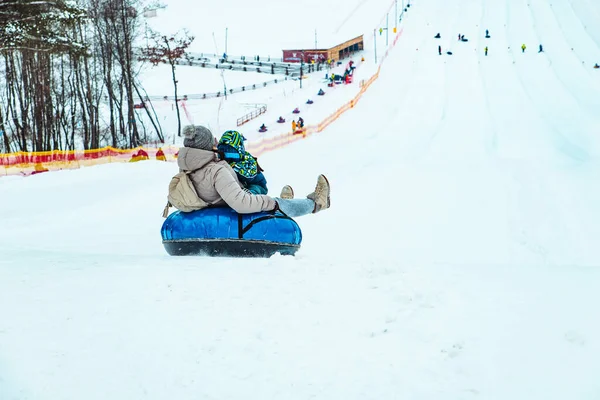 雪のチューブで雪の丘を滑り降りる子供の親 冬のレジャー — ストック写真