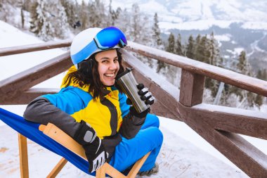 Kayak kıyafetli kadın sandalyede oturmuş, dağdaki fotokopi alanının zirvesinden panoramik manzaraya bakıyor.