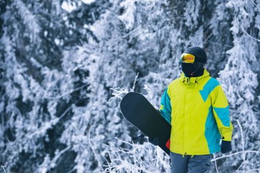 Snowboard 'lu bir adam karlı tepenin yanından geçiyor.
