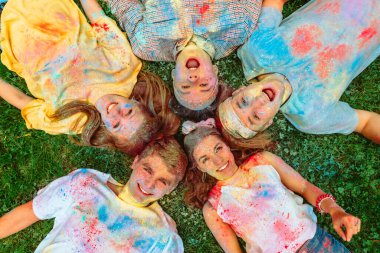 Mutlu arkadaşlar yeşil çimlere uzanmış Holi boyalarıyla kirlenmişler. Hint tatili