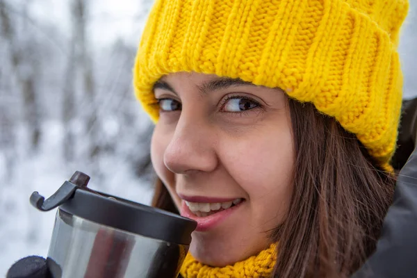smiling woman in winter outfit drinking warm up drink from refillable mug copy space