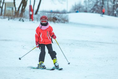 LVIV, UKRAINE - 12 Ocak 2019: Kırmızı ceketli bir çocuk tepeden aşağı kayıyor. kış aktiviteleri.