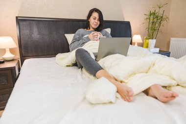 Kadın dizüstü bilgisayarda çalışıyor ve kahve içiyor.