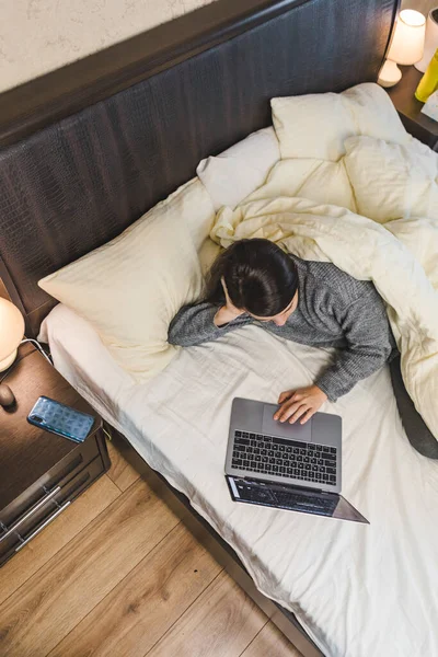 Жінка лежить в ліжку працює на ноутбуці — стокове фото
