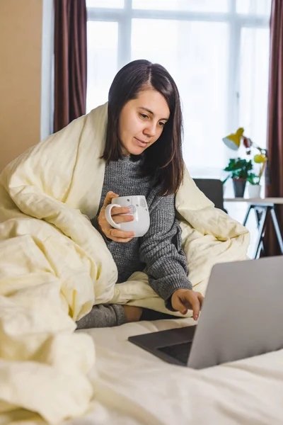 Woman working on laptop in bed and drinking coffee — Stock Photo, Image