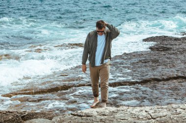 Rüzgarlı yaz tatilinde Rocky Beach 'te yürüyen bir adam. Deniz manzarasının tadını çıkar