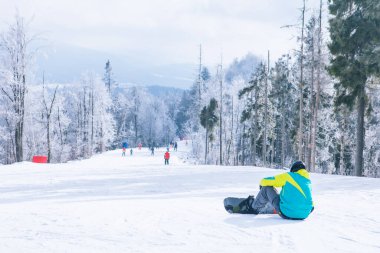 Tepede oturan adam manzaranın tadını çıkarıyor. Snowboard. Kış sporları. Boşluğu kopyala