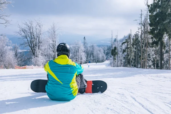 Tepede oturan adam manzaranın tadını çıkarıyor. Snowboard. Kış sporları. Boşluğu kopyala