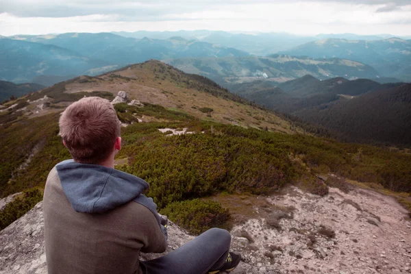 山の頂上の岩の上に座って景色を楽しんでいる若い男 ハイキングのコンセプト — ストック写真