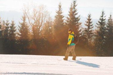 Arka planda snowboard dağlarıyla tepenin yanından geçen bir adam.