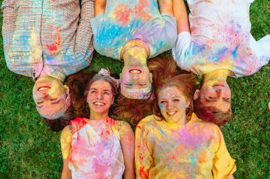 Mutlu arkadaşlar yeşil çimlere uzanmış Holi boyalarıyla kirlenmişler. Hint tatili