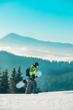 Arka planda snowboard dağlarıyla tepenin yanından geçen bir adam.