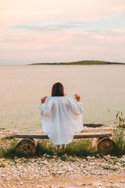 Kadın bankta oturmuş denizin üzerinde gün batımını seyrediyor. sakinlik yeri