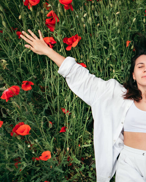 young pretty woman laying down at the field of poppy flowers. copy space. summer time