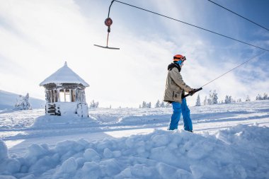 Dragobrat, Ukrayna - 11 Ocak 2021: Erkek snowboardcu kış sporu için dağların zirvesine çıkmak için kayak boyunduruğu kullanıyor.