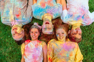 Mutlu arkadaşlar yeşil çimlere uzanmış Holi boyalarıyla kirlenmişler. Hint tatili