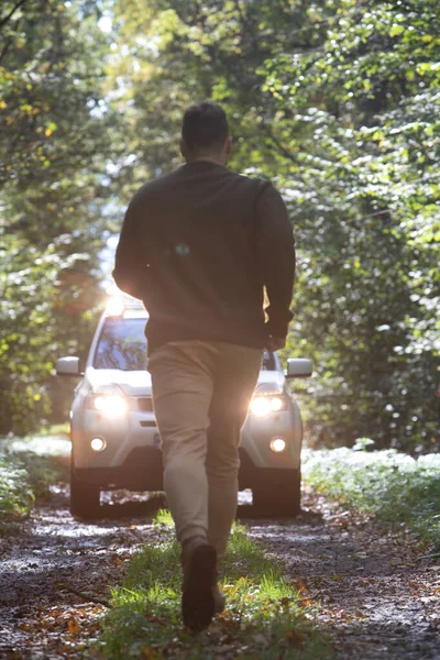 man running to car standing at the forest trail with headlights turned on