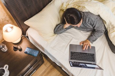 Kadın yatağa uzanıp dizüstü bilgisayarda serbest çalışma kavramı üzerinde çalışıyor.