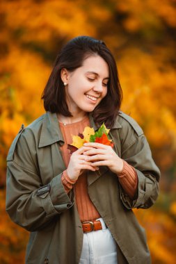 Altın sonbahar yapraklarının önünde gülümseyen güzel kadın.
