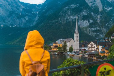 Sarı yağmurluklu kadın Hallstatt City panoramik manzarasına bakıyor