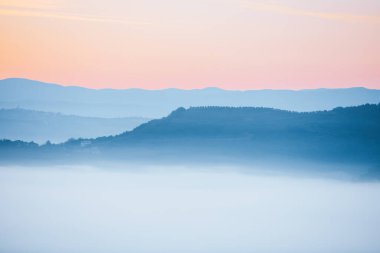 Güneşin dağların üzerindeki doğuşunu sisli ve tepe noktalarının altındaki bulutları