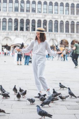 Beyaz şapkalı kadın Venice City Meydanı San Marco 'da güvercinlerle eğleniyor.