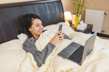 Telefonunu kullanan kadın dizüstü bilgisayarda çalışıyor ve fotokopi odasında uzanıyor.