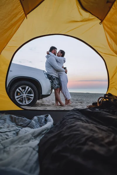 couple meeting sunrise at sea beach. view through camping tent. summer vacation