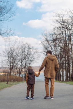 Baba oğul el ele tutuşarak parkta yürüyorlar. arka plan