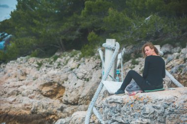 Kenarda oturan kadın deniz manzaralı asma köprü resmi çiziyor.