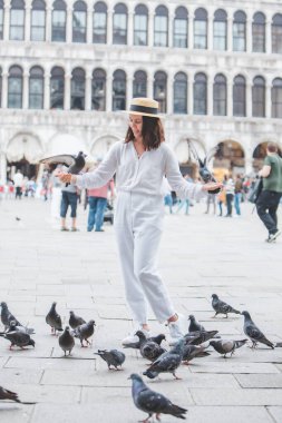 Beyaz şapkalı kadın Venice City Meydanı San Marco 'da güvercinlerle eğleniyor.