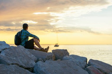 Sırt çantalı bir adam gün batımını seyrediyor. Boşluğu kopyala