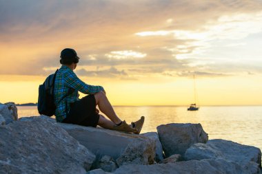 Sırt çantalı bir adam gün batımını seyrediyor. Boşluğu kopyala