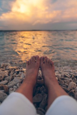 Sahilde uzanmış denizin üstünde gün batımını seyreden bir kadın. vücut parçaları bacaklar