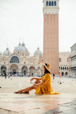 Kadın merdivenlerde oturmuş Aziz Marco Meydanı 'na bakıyor güneşli yaz günü çan kulesi Aziz Marco Bazilikası' nda.