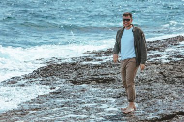 Rüzgarlı yaz tatilinde Rocky Beach 'te yürüyen bir adam. Deniz manzarasının tadını çıkar. yaz zamanı