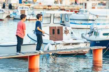 Fazana, Hırvatistan - 1 Haziran 2019: iki küçük çocuk deniz tahtası iskelesinde balık tutuyor. deniz rıhtımı