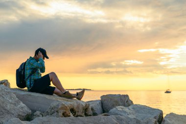 Sırt çantalı bir adam gün batımını seyrediyor ve müzik dinliyor. Boşluğu kopyala